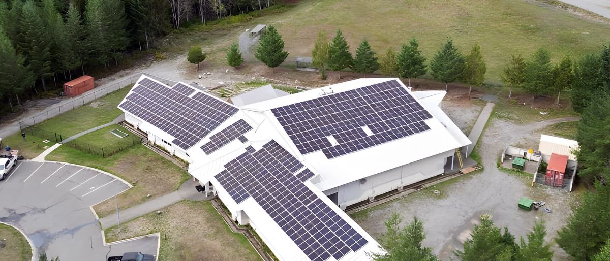 Aerial view of Yuquot School, Mowachaht/Muchalaht First Nation, with rooftop solar panels and forest on every side